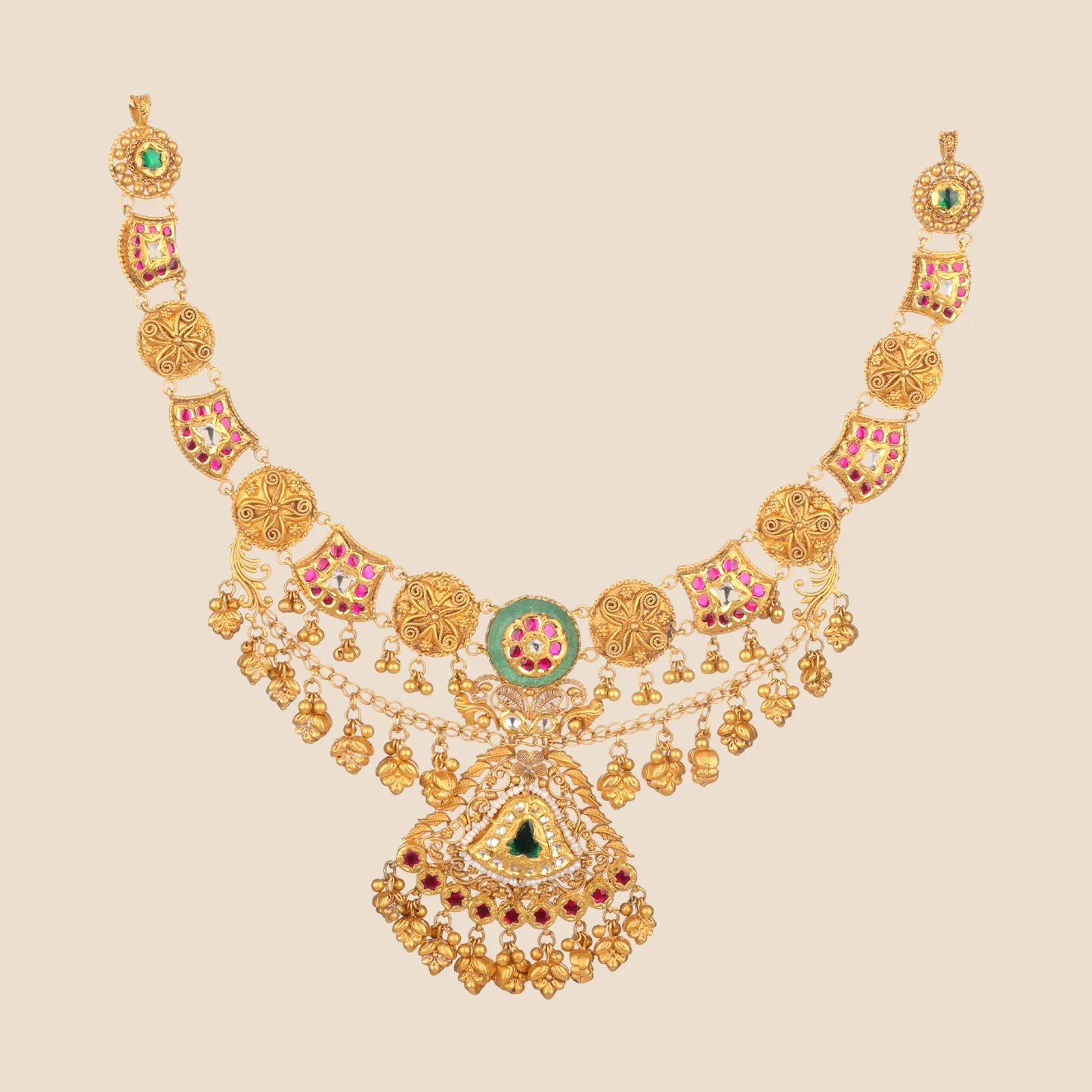 A detailed gold choker necklace featuring a large triangular pendant with green and red gemstones, intricate filigree, and dangling gold charms.