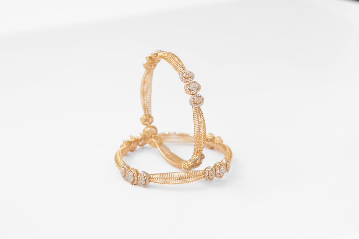 Pair of gold bangles with intricate designs on a white background