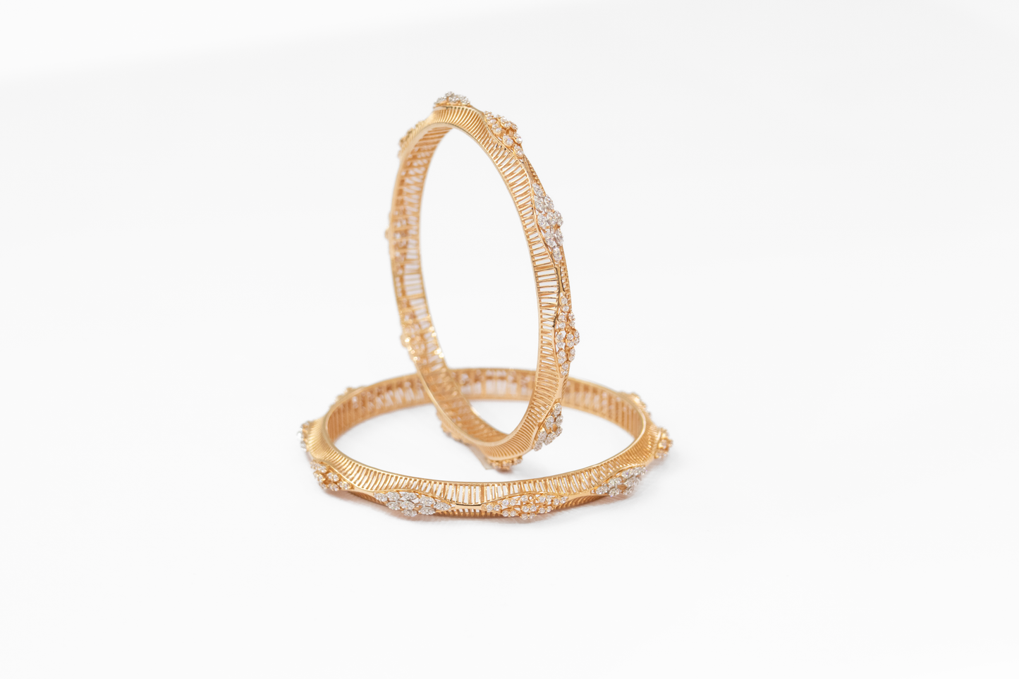 Pair of gold bangles with intricate designs on a white background