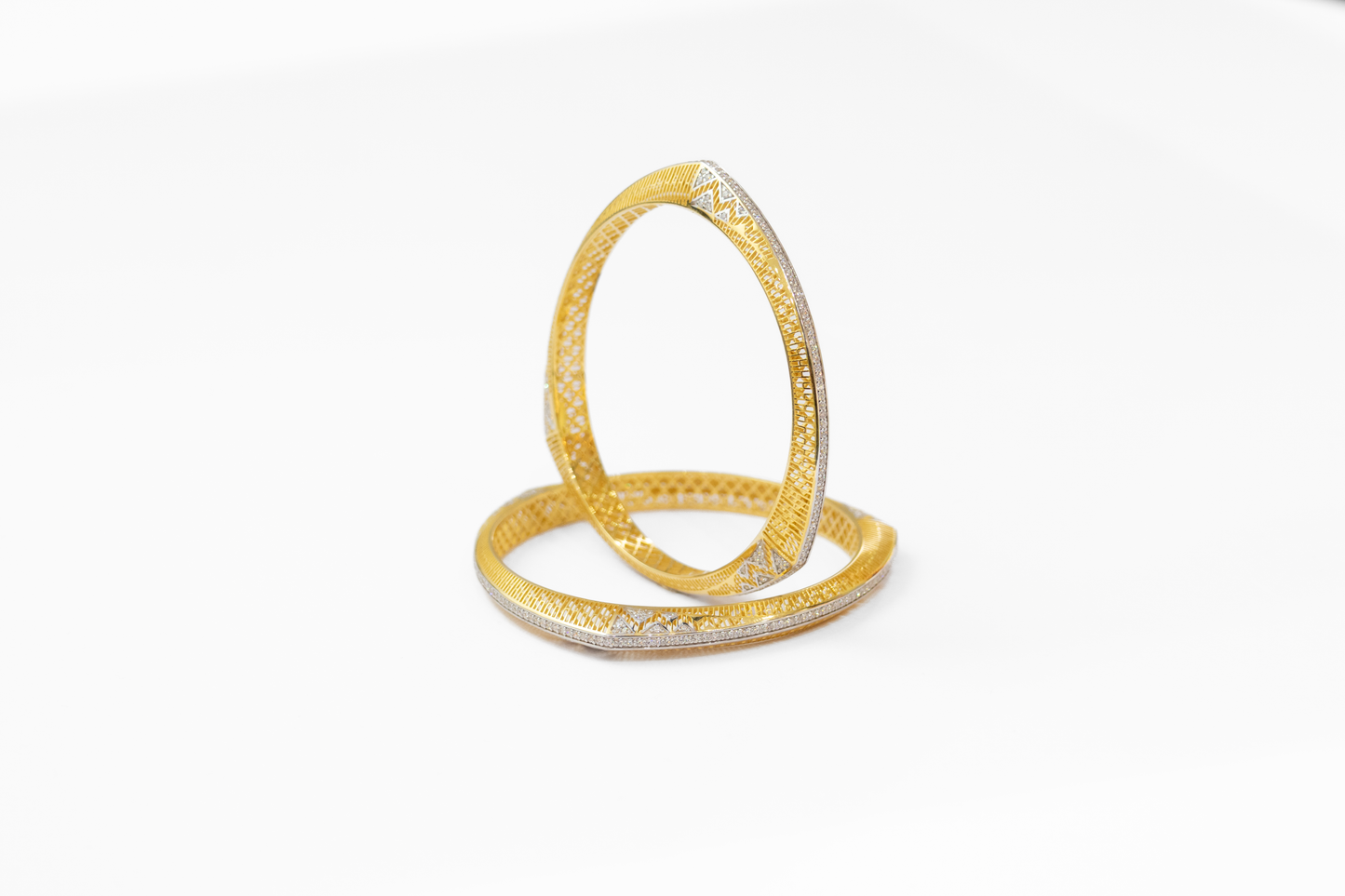 Two gold bangles with intricate designs on a white background